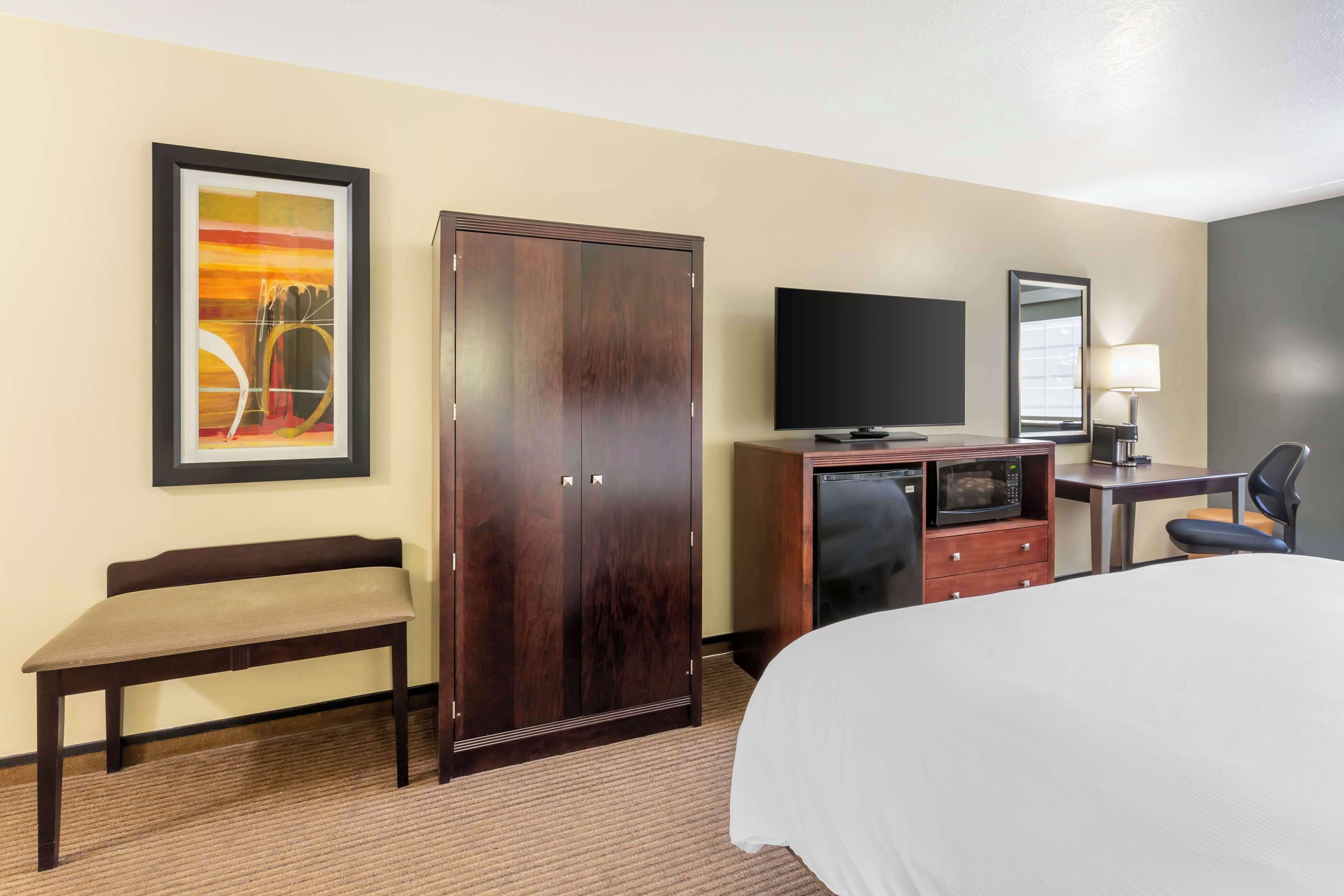 Une chambre d’hôtel comprenant un lit, un bureau avec un ordinateur, une télévision, une armoire et un banc.