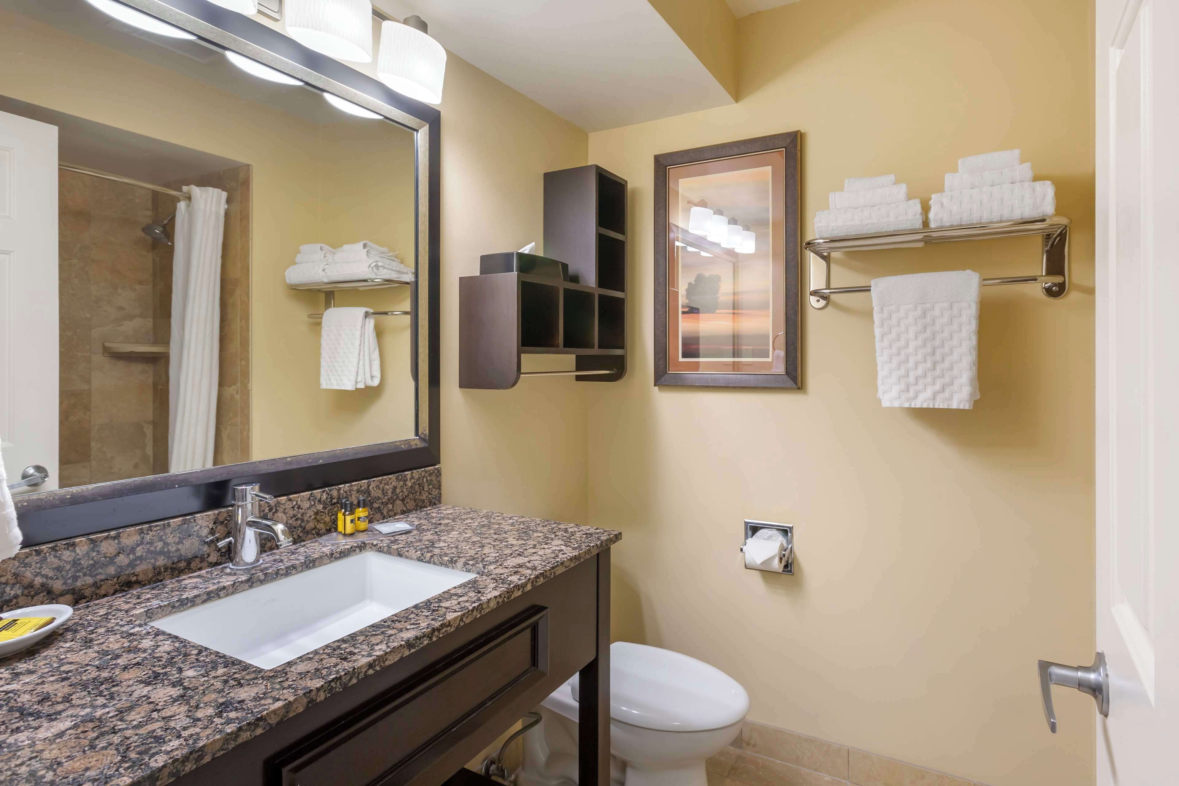 A bathroom with a granite countertop sink, a mirror, a towel rack, and a toilet.