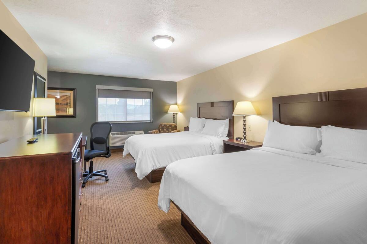 Une chambre d’hôtel avec deux lits, un bureau, une chaise et une fenêtre.