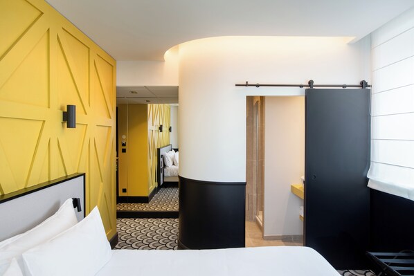 A hotel room with a bed, a large pillar, a sliding door, and a patterned floor.