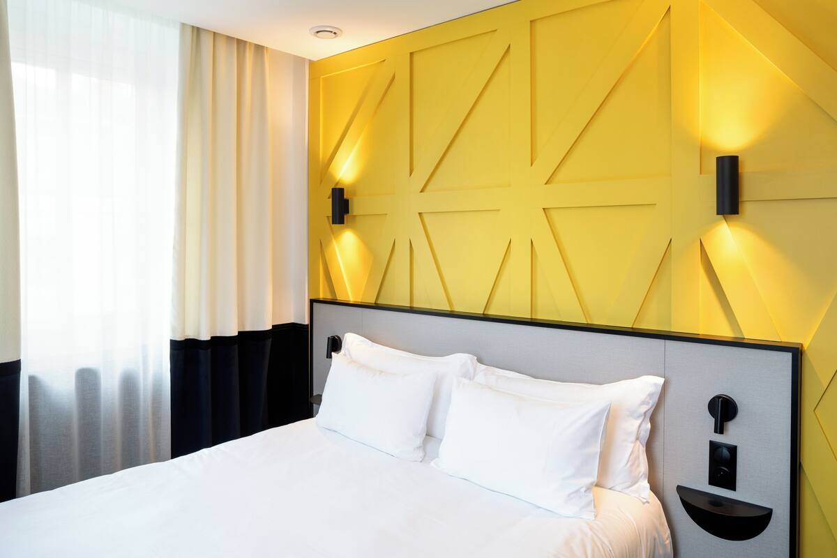 A modern hotel room with a large bed, a geometric wall design, and two bedside tables with lamps.