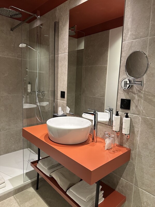 A modern bathroom with a large oval sink, a handheld showerhead, and a glass-enclosed shower.