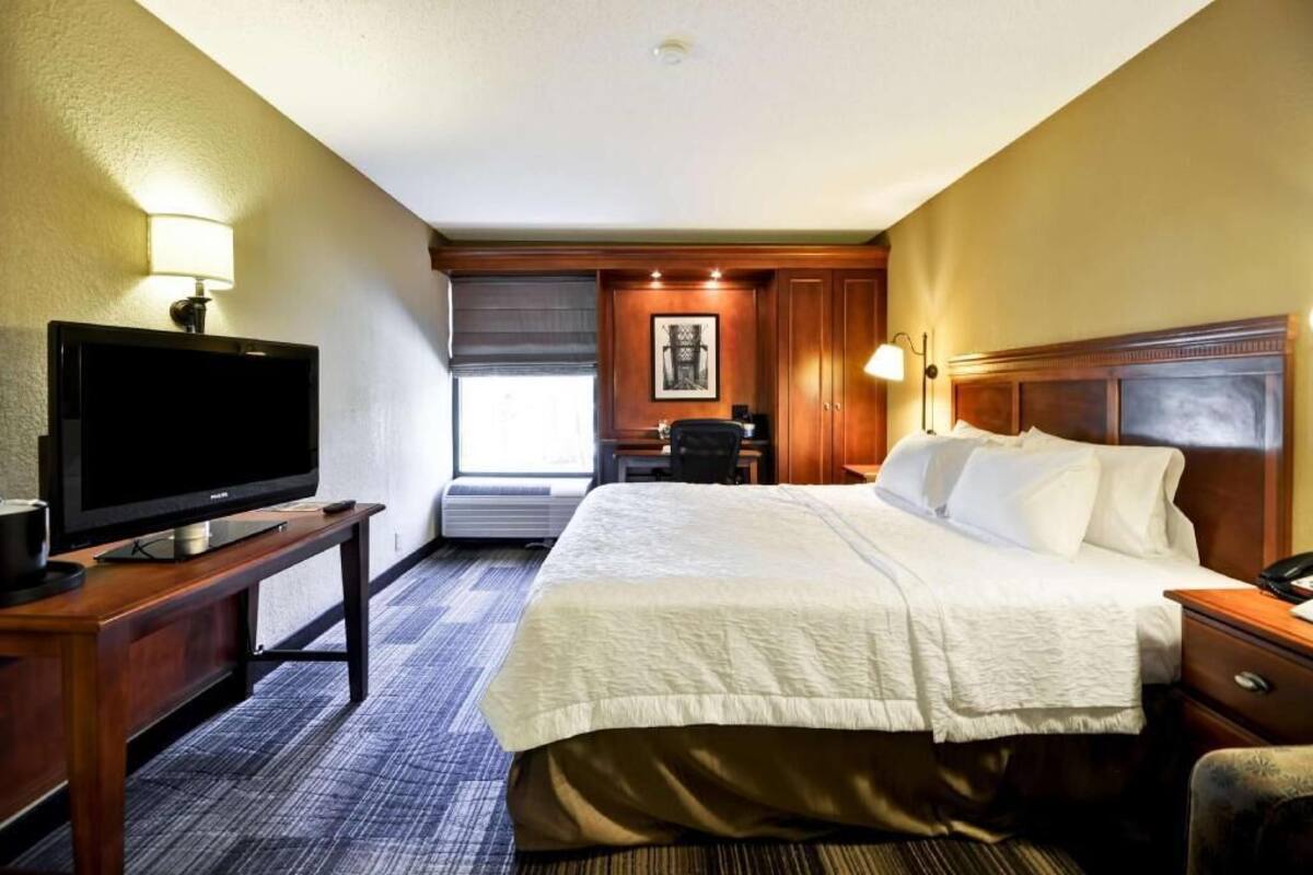 A hotel room with a bed, a TV on a stand, a desk, and a chair.