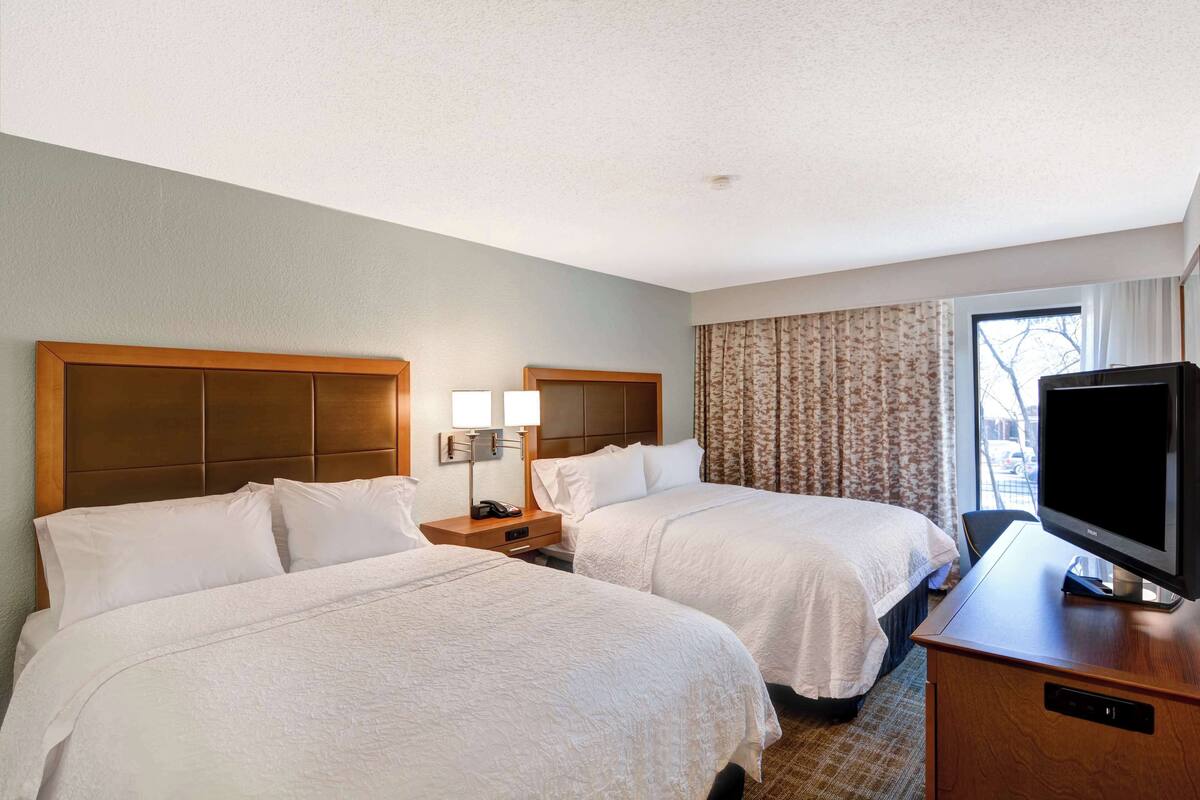 A hotel room with two beds, a TV, a desk, and a window with curtains.