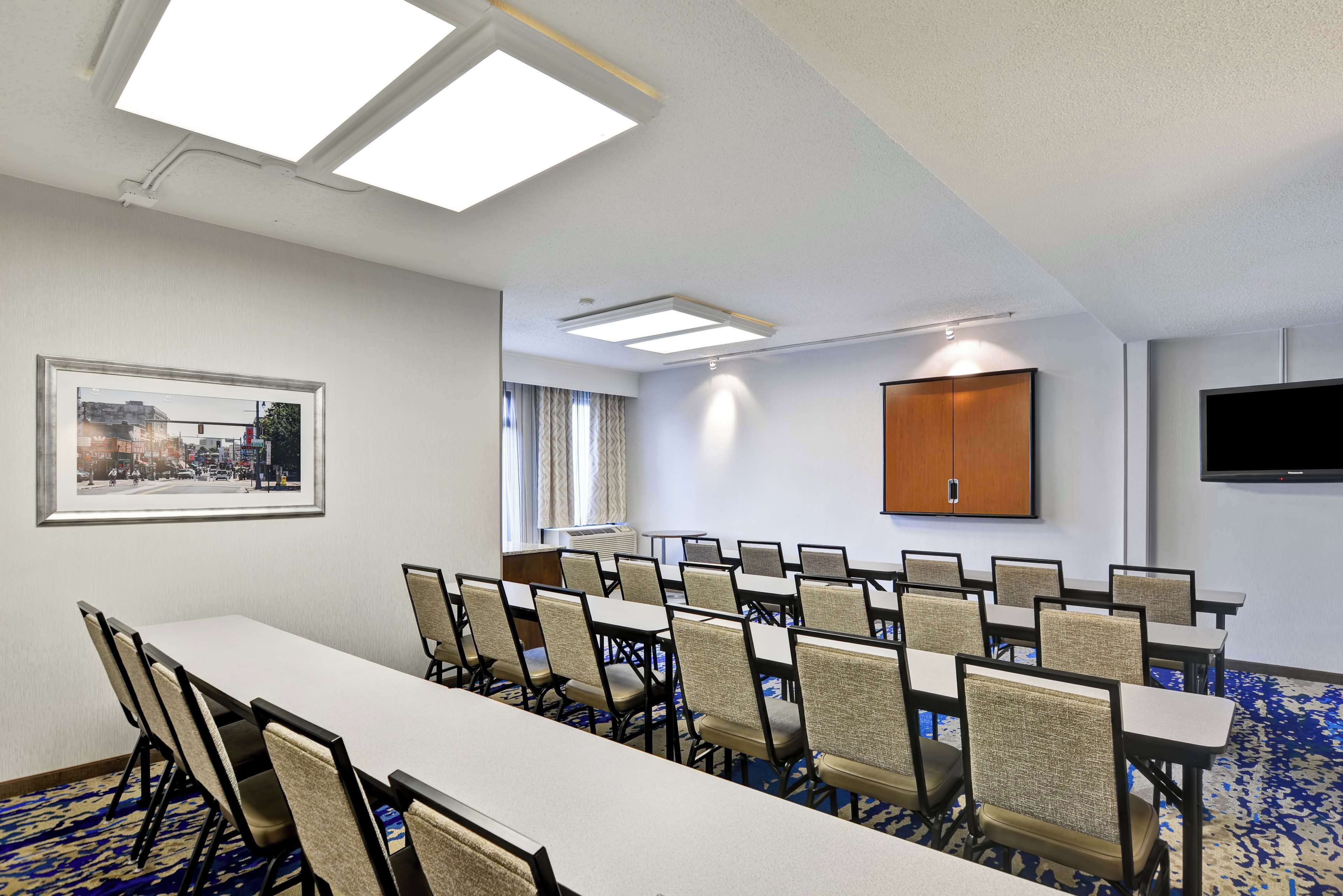 Une salle de conférence avec une longue table, des chaises, un tableau encadré, un meuble et un téléviseur fixé au mur.