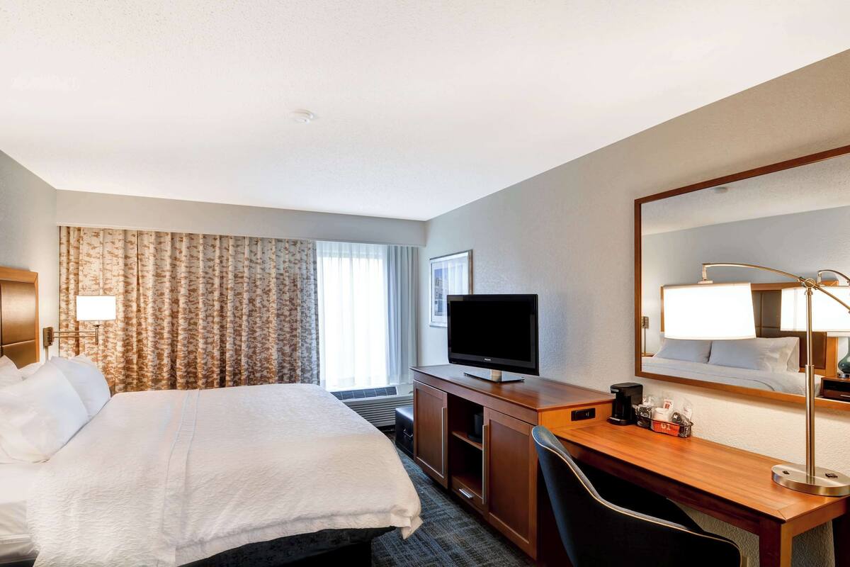 A hotel room with a large bed, a desk with a computer, a TV, and a mirror.