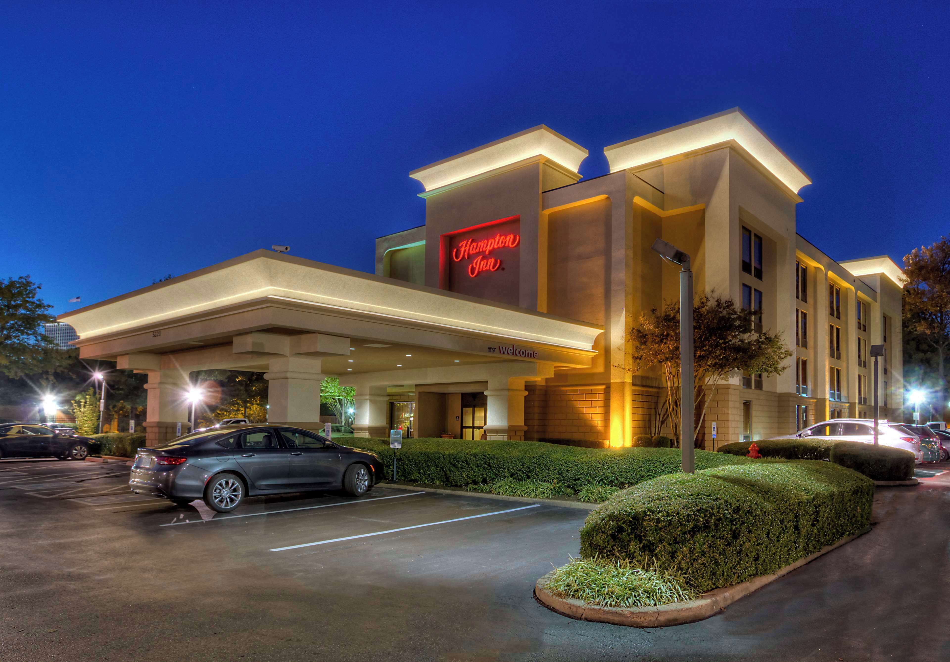 A modern hotel with a prominent neon sign, a welcoming entrance, and a parking lot.