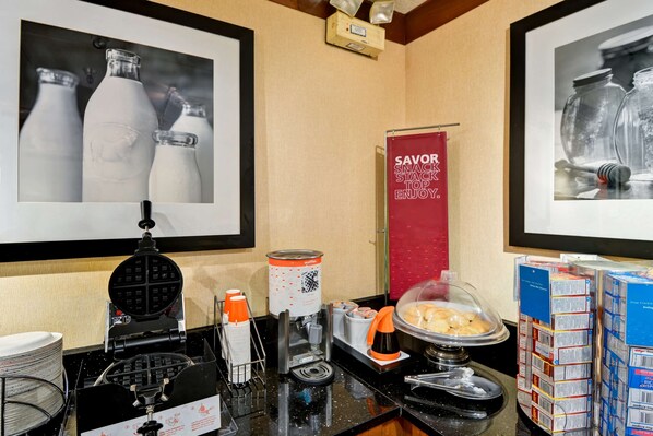 A breakfast bar with waffle maker, coffee station, and food display.
