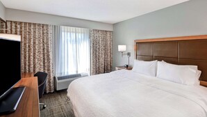 A hotel room with a large bed, a desk with a computer, a TV, a bedside table with a lamp, and a window with curtains. - Hampton Inn Memphis-Poplar (Memphis)