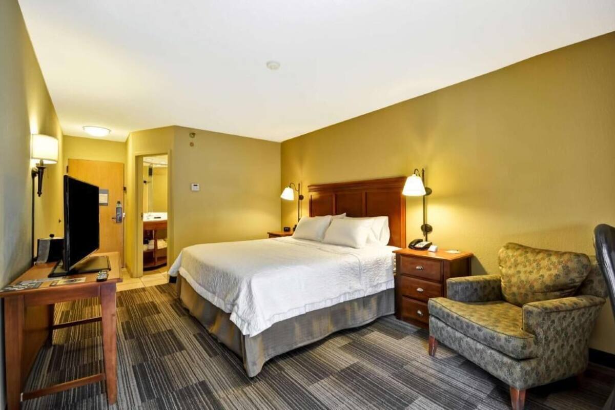 A hotel room with a bed, a TV, a chair, and a desk.