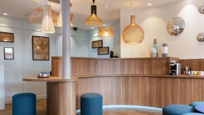 A modern reception area with wooden reception desk, blue cushioned stools, and pendant lighting. - Hotel Des Nations Saint Germain (Paris)