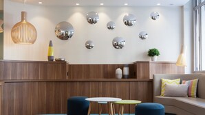 A modern lobby with a wooden reception desk, round mirrors, and a seating area with ottomans and tables. - Hotel Des Nations Saint Germain (Paris)