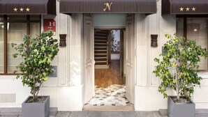 A hotel entrance with a staircase leading inside, potted plants on either side, and a tiled floor. - Hotel Des Nations Saint Germain (Paris)