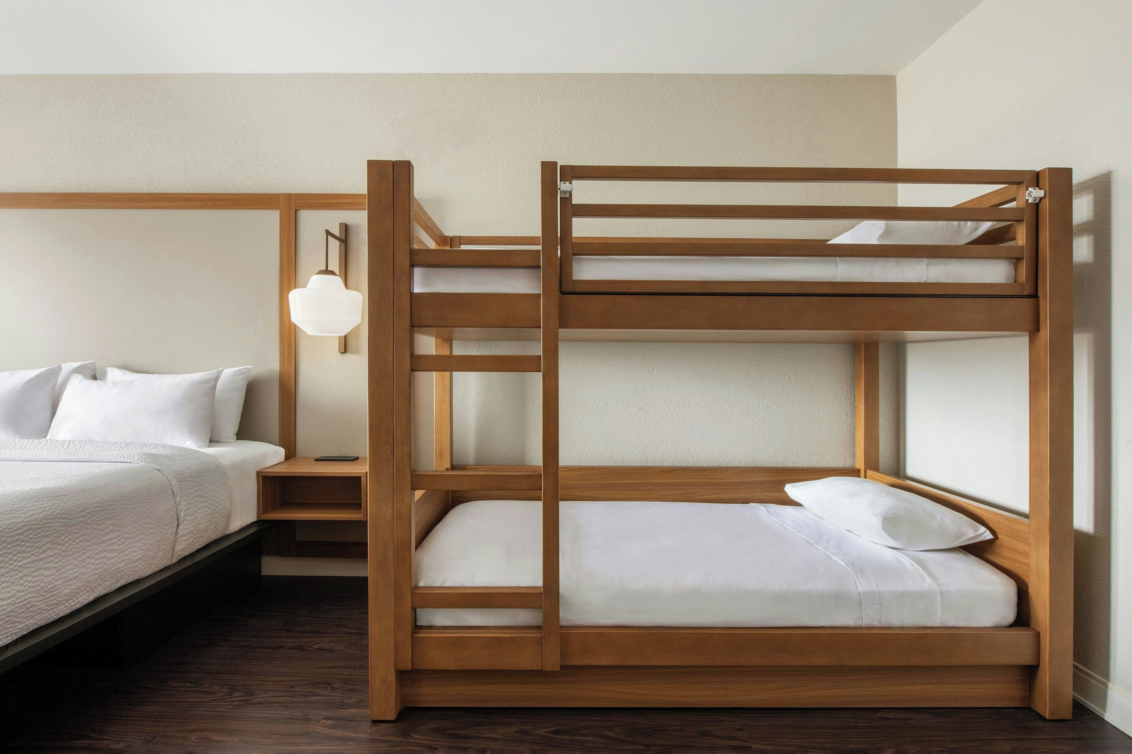 A bunk bed with a wooden frame, a bedside table, and a lamp.