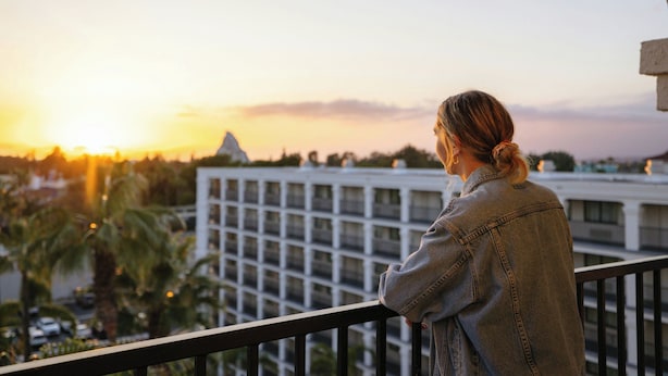 A person standing on a balcony overlooking a cityscape during sunset.