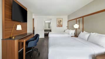 Habitación de hotel con escritorio, dos camas, televisor y baño visible a través de una puerta abierta.