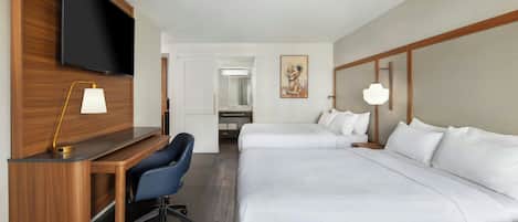 Habitación de hotel con escritorio, dos camas, televisor y baño visible a través de una puerta abierta.