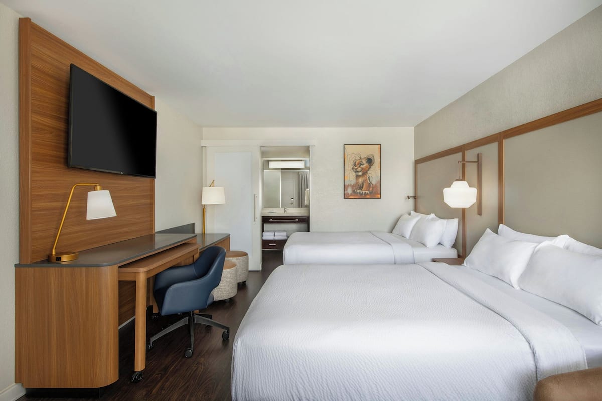Una habitación de hotel con escritorio, dos camas, televisión y un cuadro.