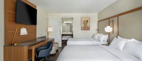 A hotel room with a desk, two beds, a TV, and a painting.