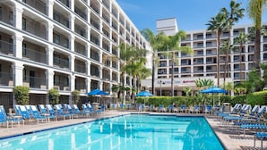 A hotel with a swimming pool surrounded by blue lounge chairs and palm trees.