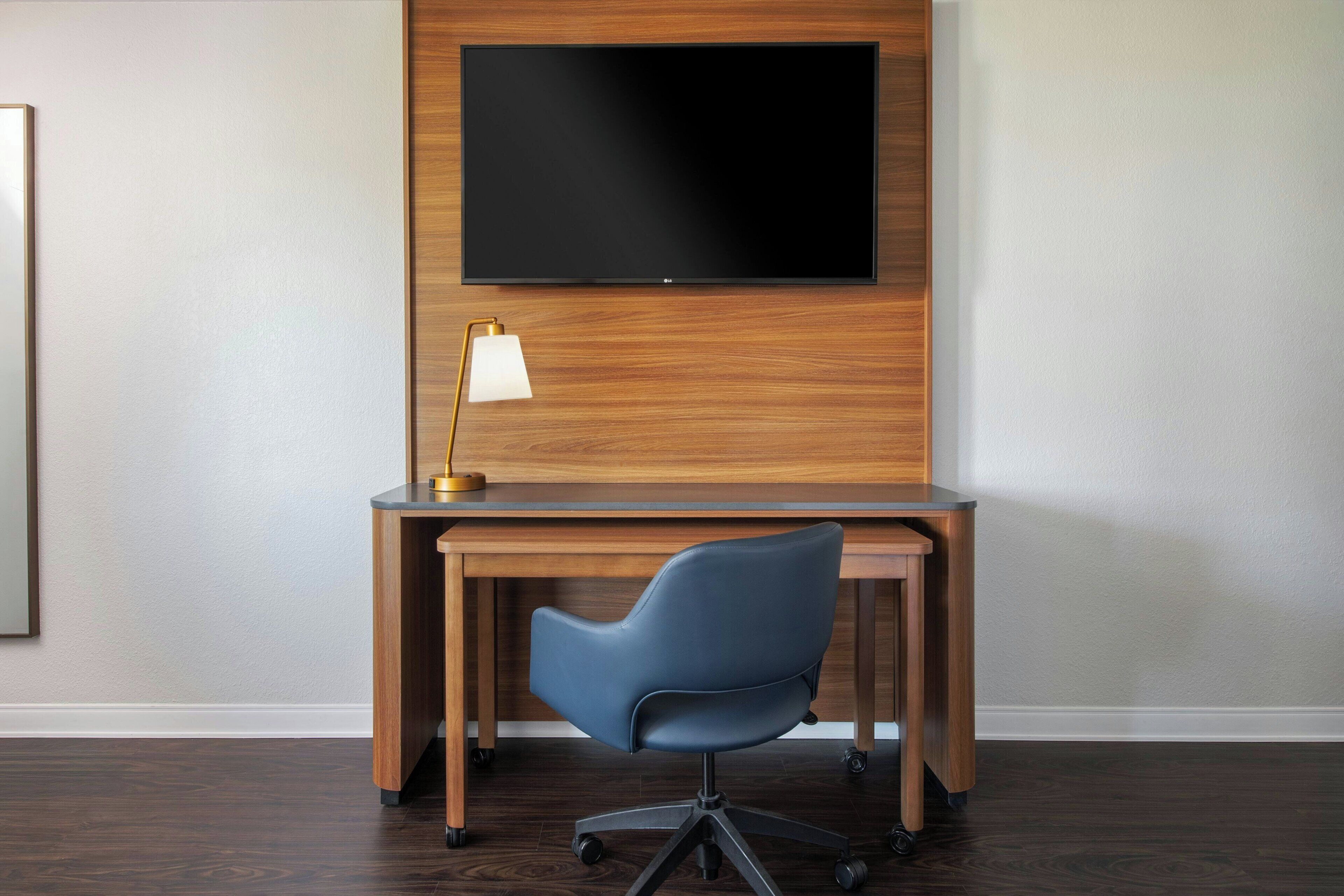 A modern office space with a wooden desk, a blue office chair, and a mounted flat-screen TV.