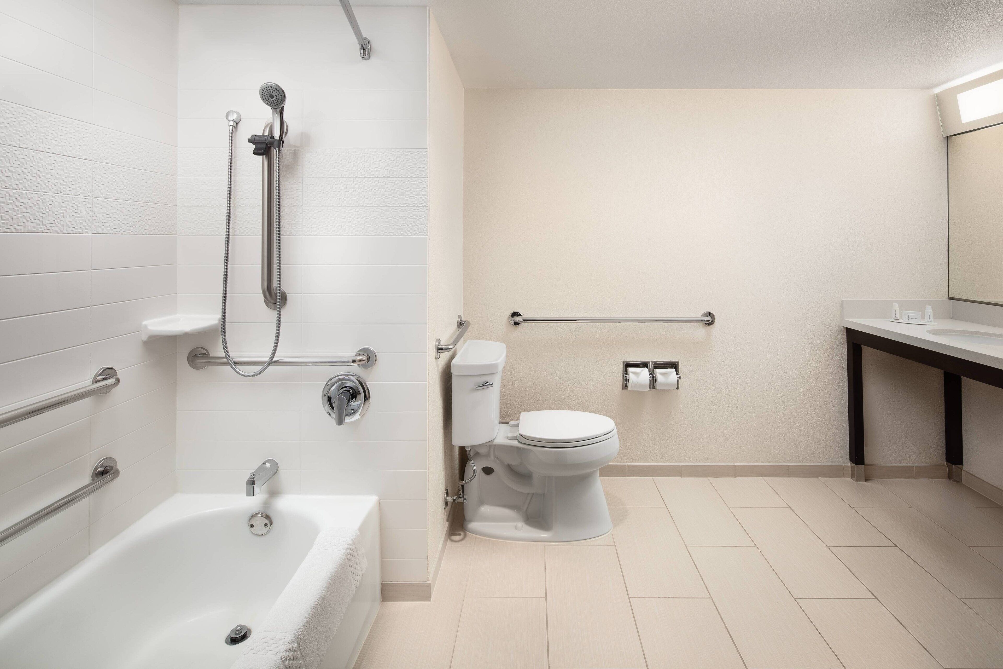 A modern bathroom with a bathtub, shower, toilet, and a handrail.