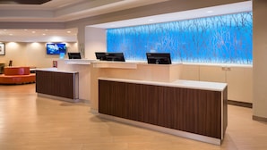 A reception area with a modern design, featuring a wooden reception desk, a large digital screen, and a wall with a blue abstract pattern.