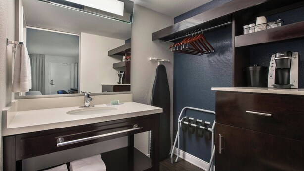 A modern bathroom with a large mirror, a sink, a towel rack, and a coffee maker.