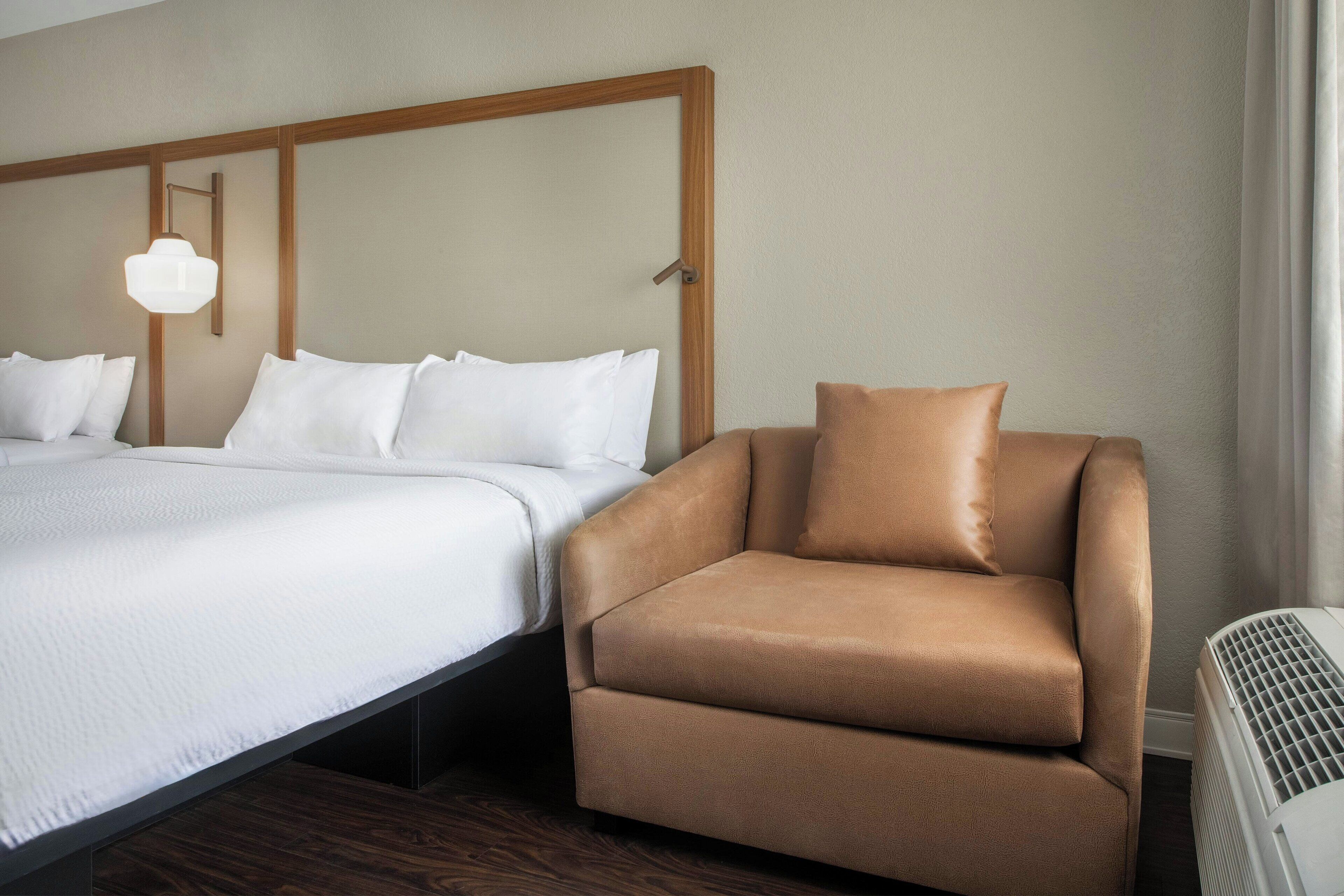 A hotel room with a bed, a sofa, a bedside table, and a wall-mounted light fixture.