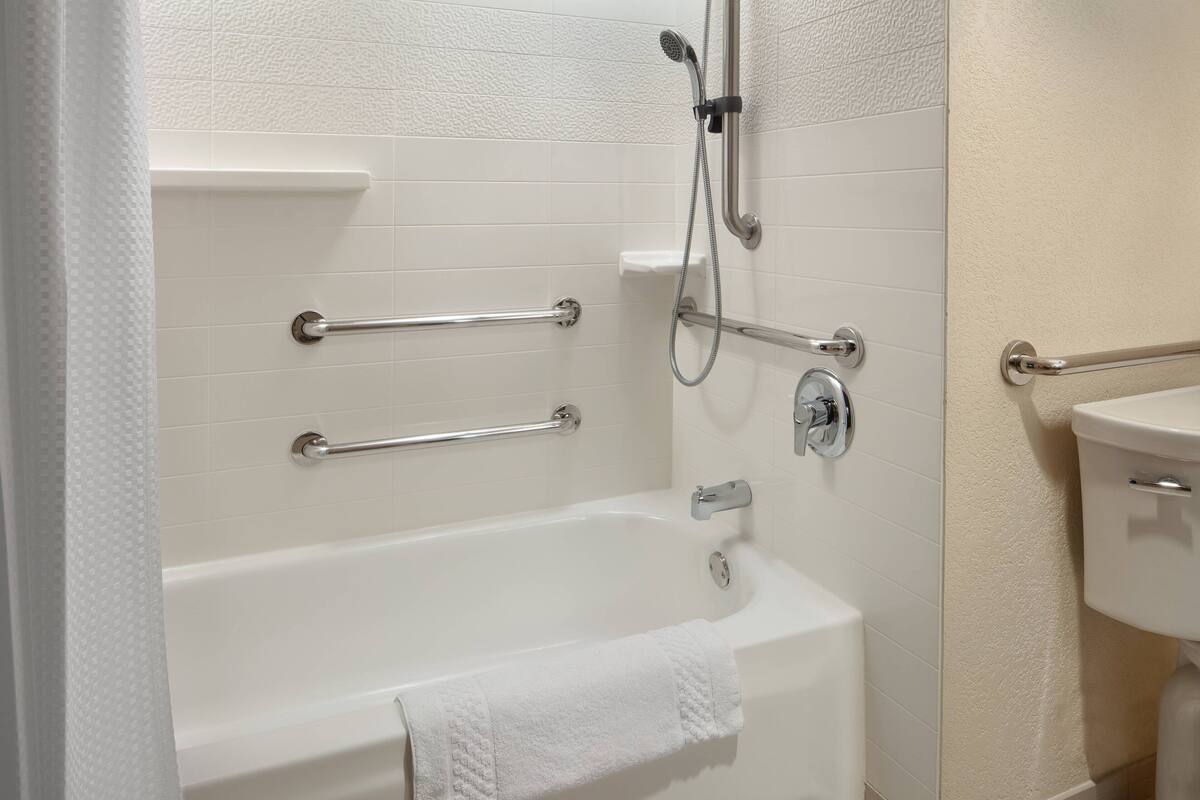 Un baño con bañera, barras de apoyo, cabezal de ducha y un inodoro.