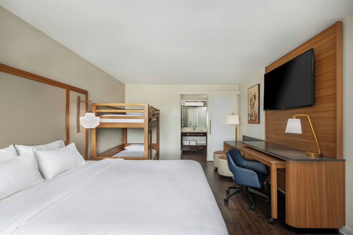Habitación de hotel con una cama grande, un escritorio con computadora, televisor y baño visible a través de una puerta abierta.