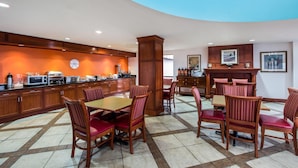 A hotel dining area with wooden furniture, a kitchen in the background, and a blue accent wall.