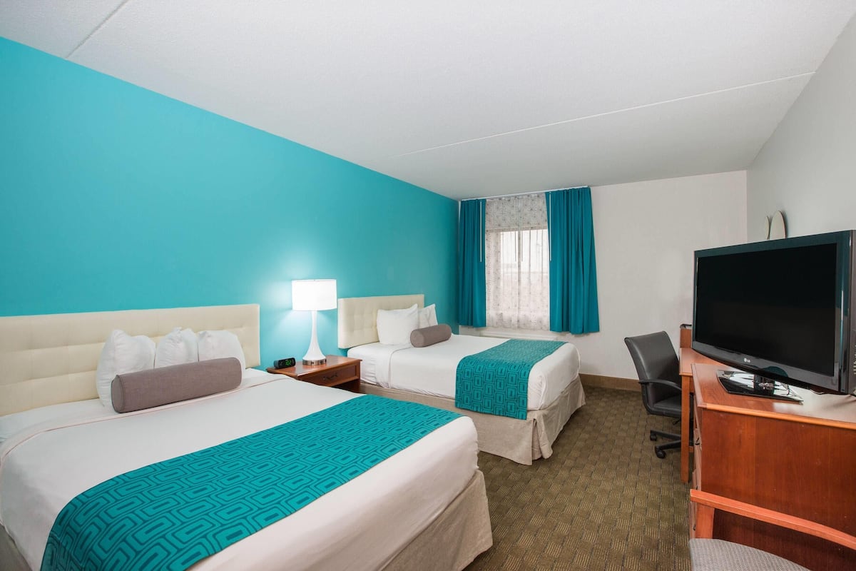 A hotel room with two beds, a desk with a TV, and a window with curtains.