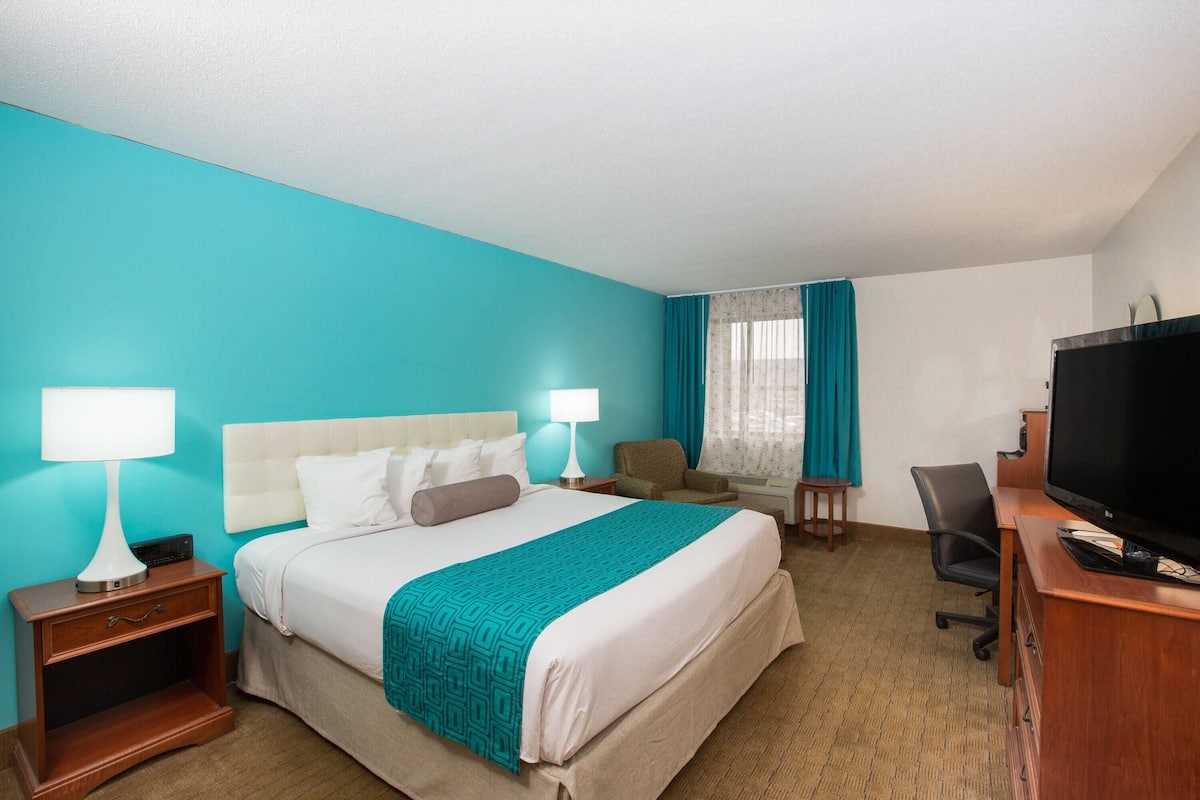 A hotel room with a bed, two bedside tables with lamps, a desk with a television, and a chair.