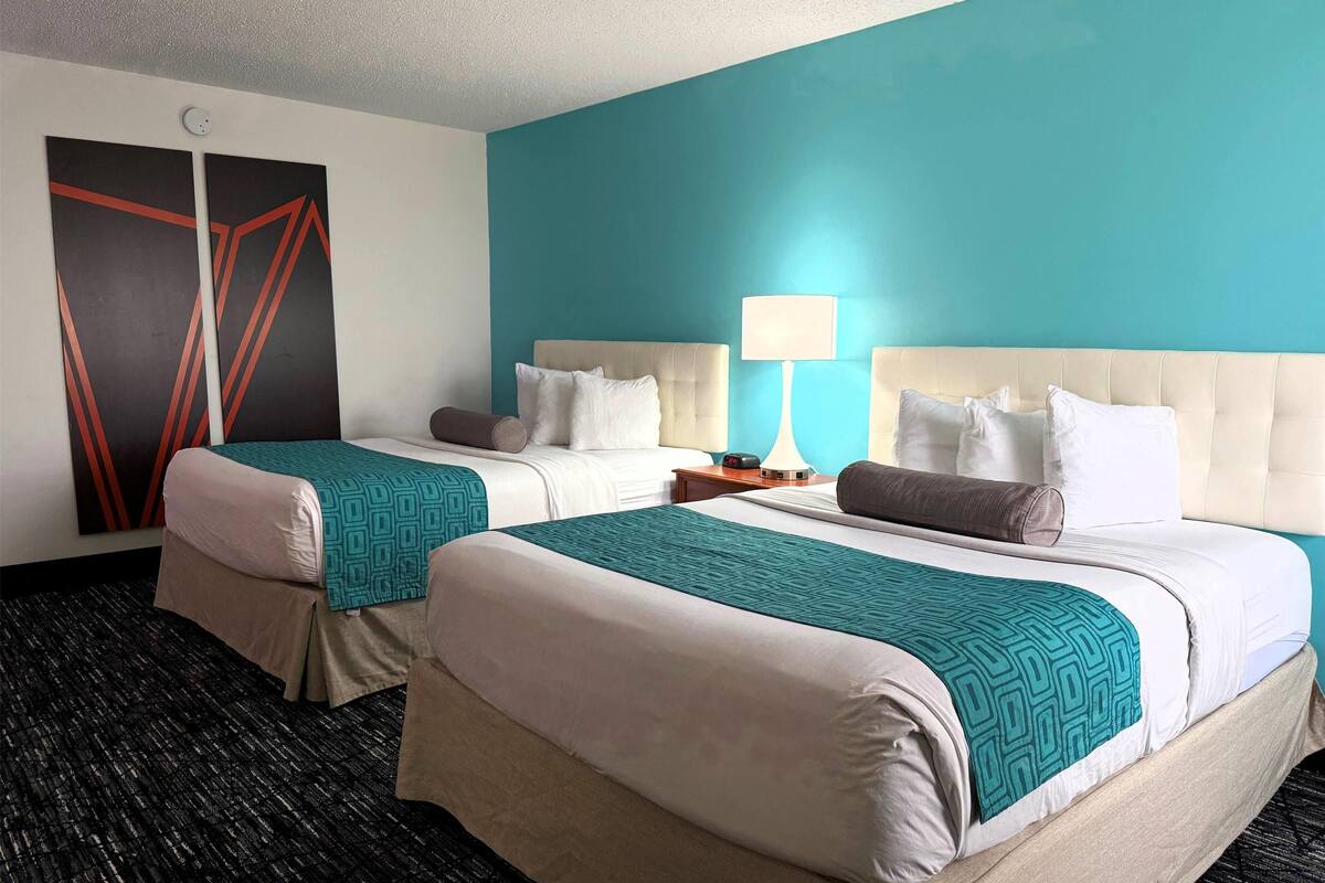 A hotel room with two beds, a teal accent wall, and a modern design.