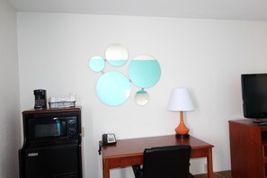 Quarto compacto com uma secretária de madeira, micro-ondas preto, telefone, abajur e televisão.