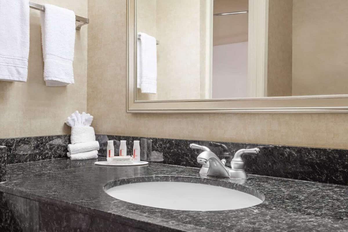 A bathroom with a marble countertop, a sink, a mirror, and a towel rack.