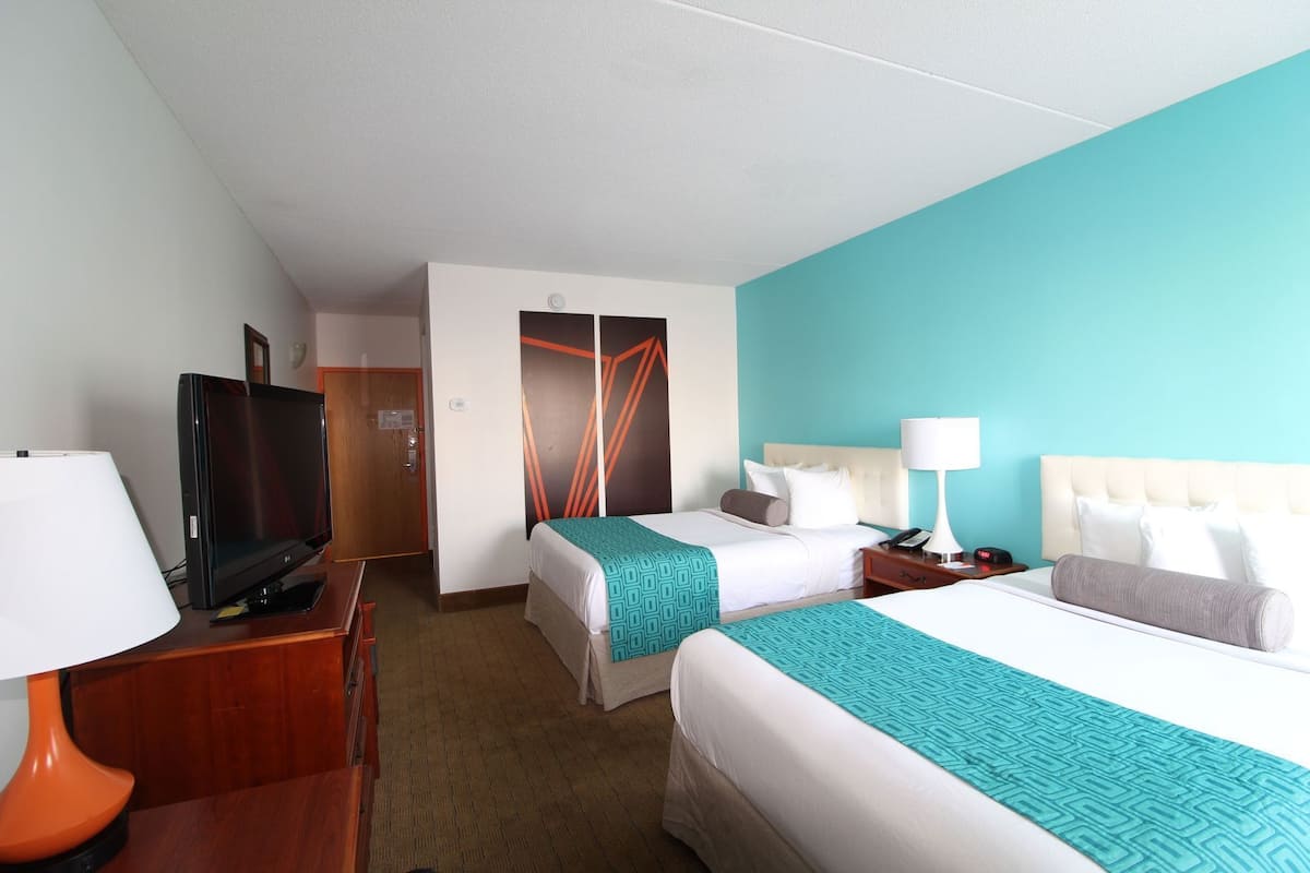 A hotel room with two beds, a television, a desk, and a door leading to another room.