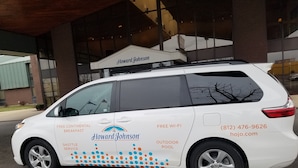 A white van with "Howard Johnson" branding, offering shuttle service, free continental breakfast, free Wi-Fi, and an outdoor pool.