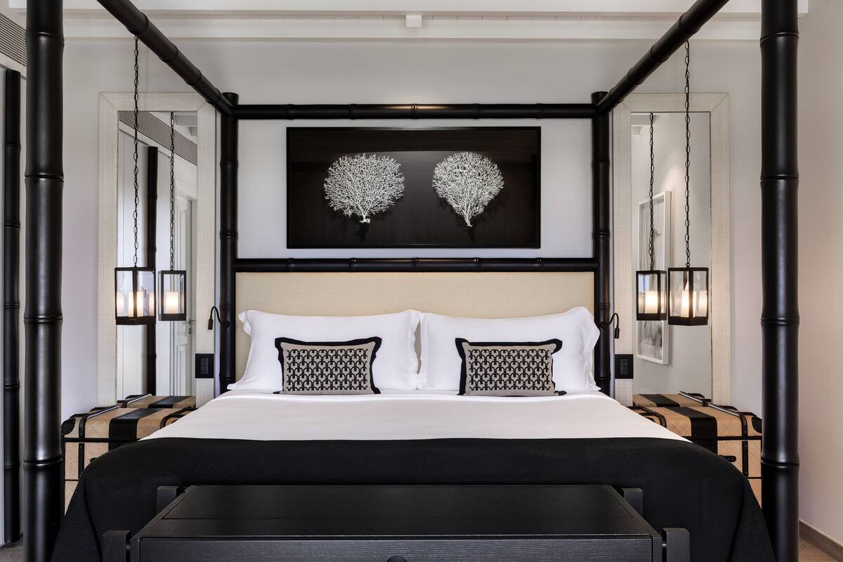 A modern hotel room with a large bed, black and white patterned pillows, a black headboard, and a framed artwork above the bed.