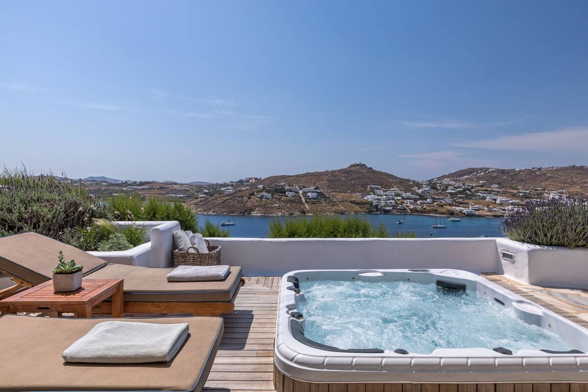 A rooftop terrace with a hot tub, lounge chairs, and a view of a coastal town.
