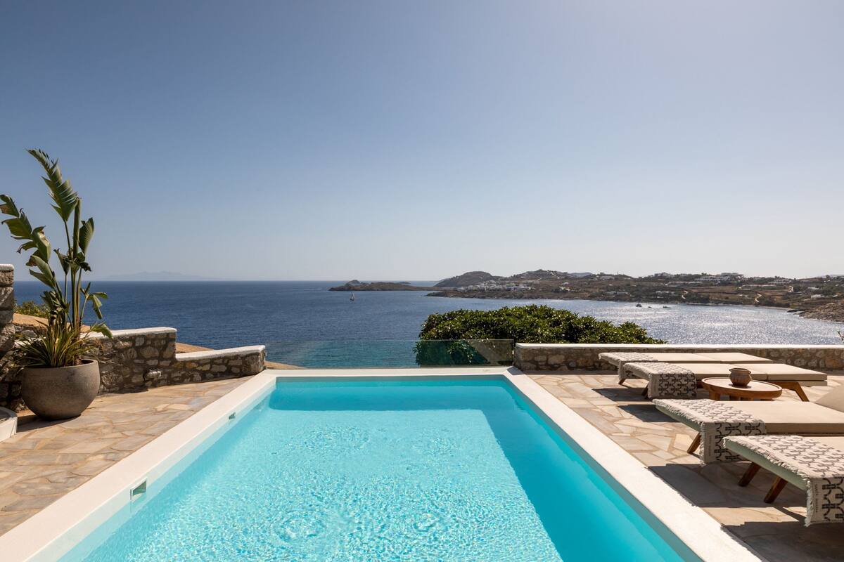 A pool with a view of the sea, stone flooring, and outdoor furniture.