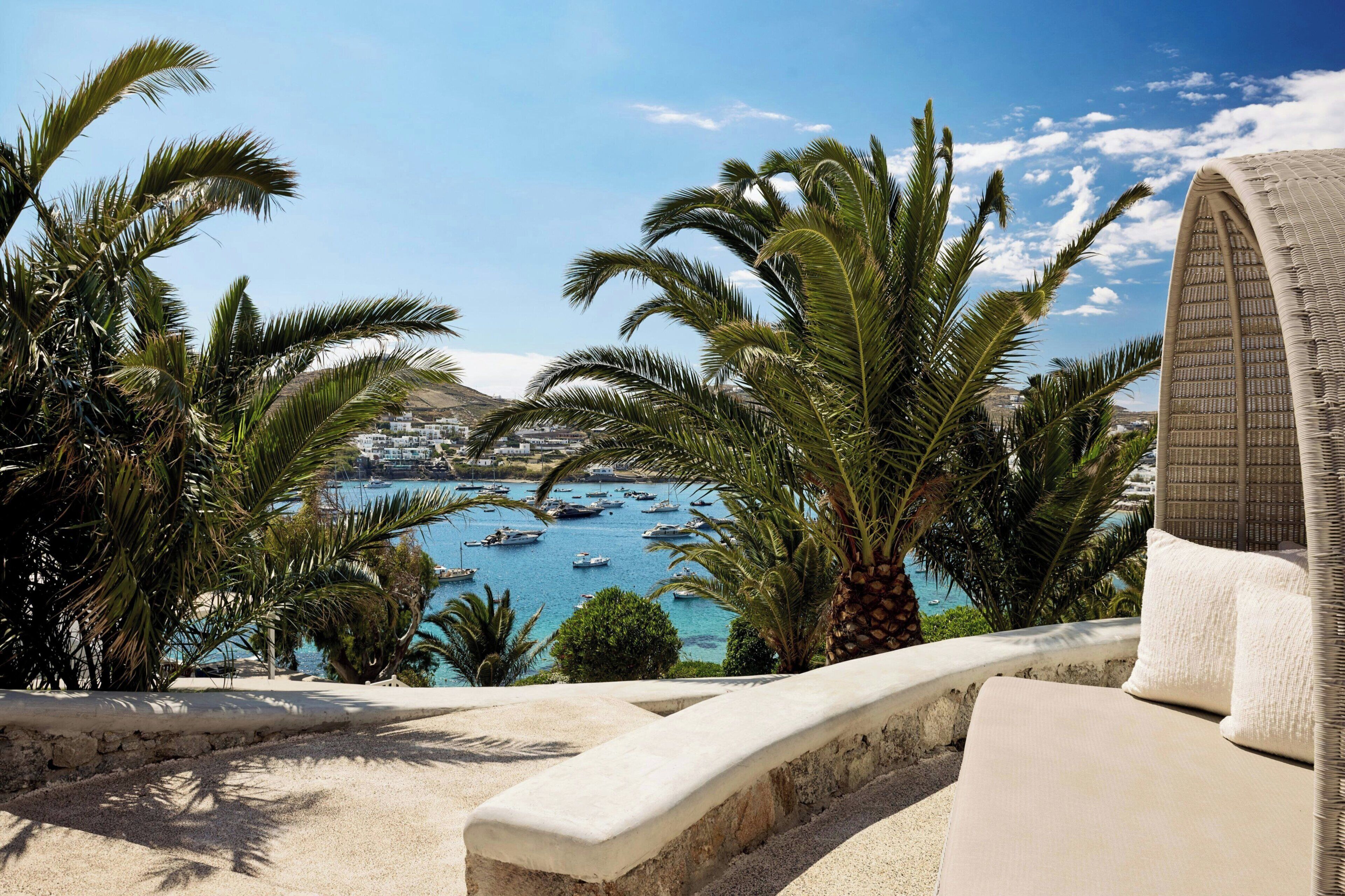 A seaside view with palm trees, a beach, and boats in the water.