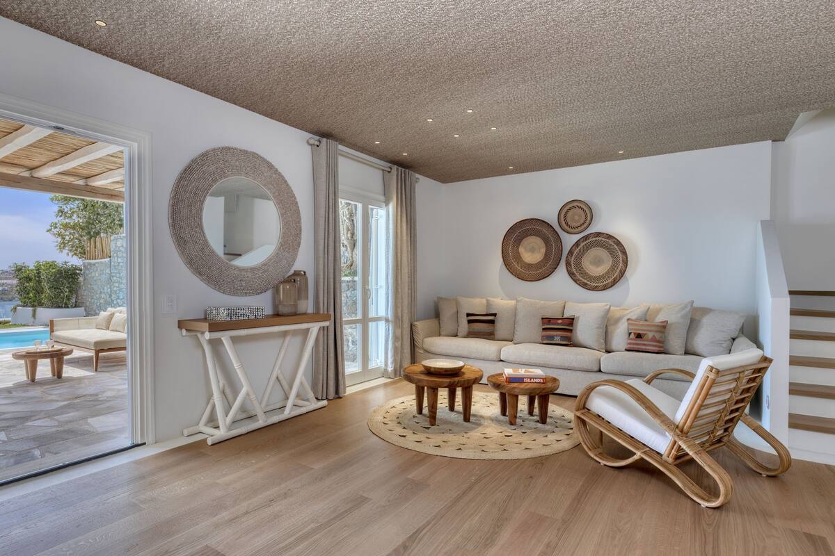 A modern living room with a wooden floor, a sofa set, a wicker chair, and a round mirror on the wall.