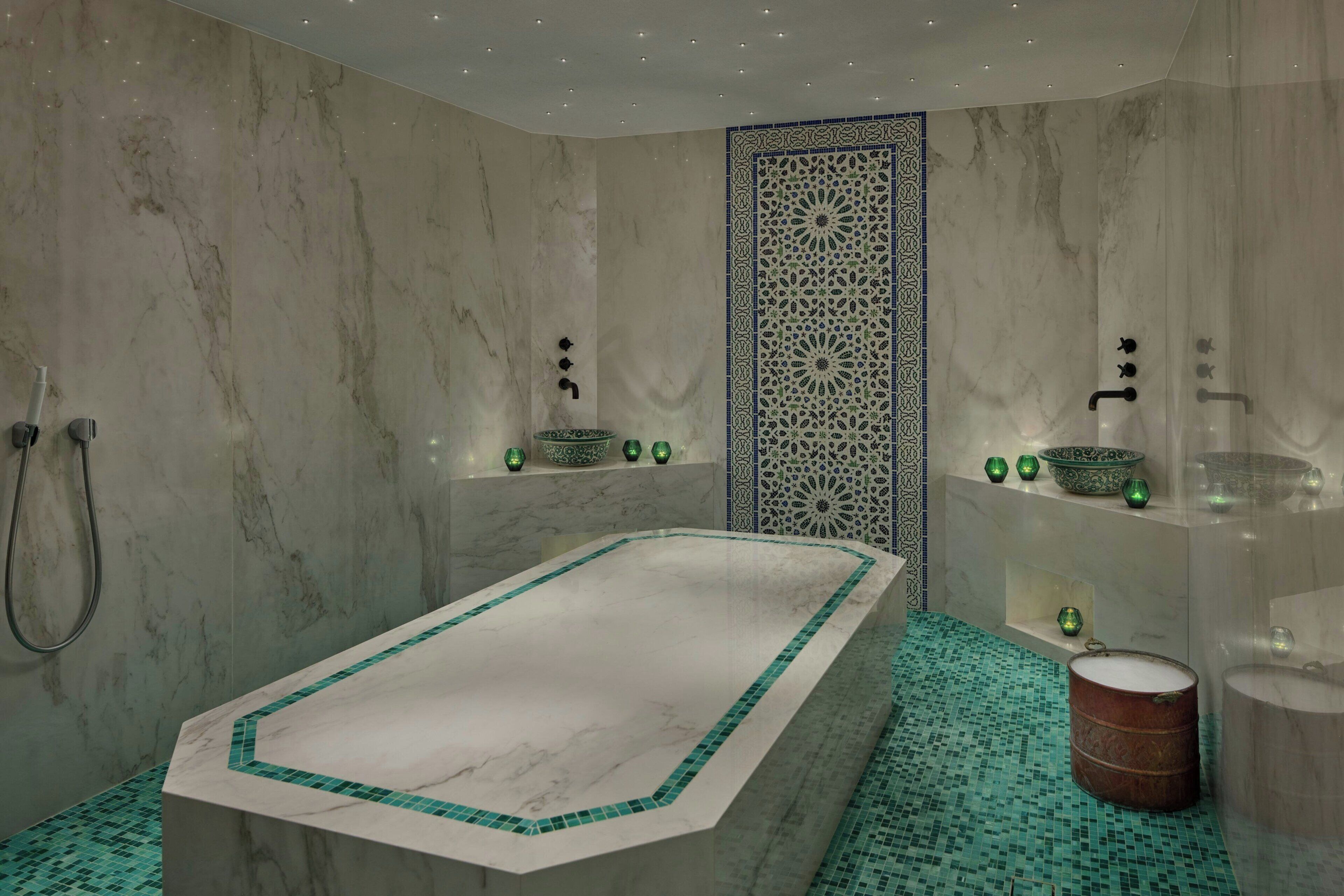 A modern bathroom with a marble bathtub, green mosaic tiles, and decorative bowls on shelves.