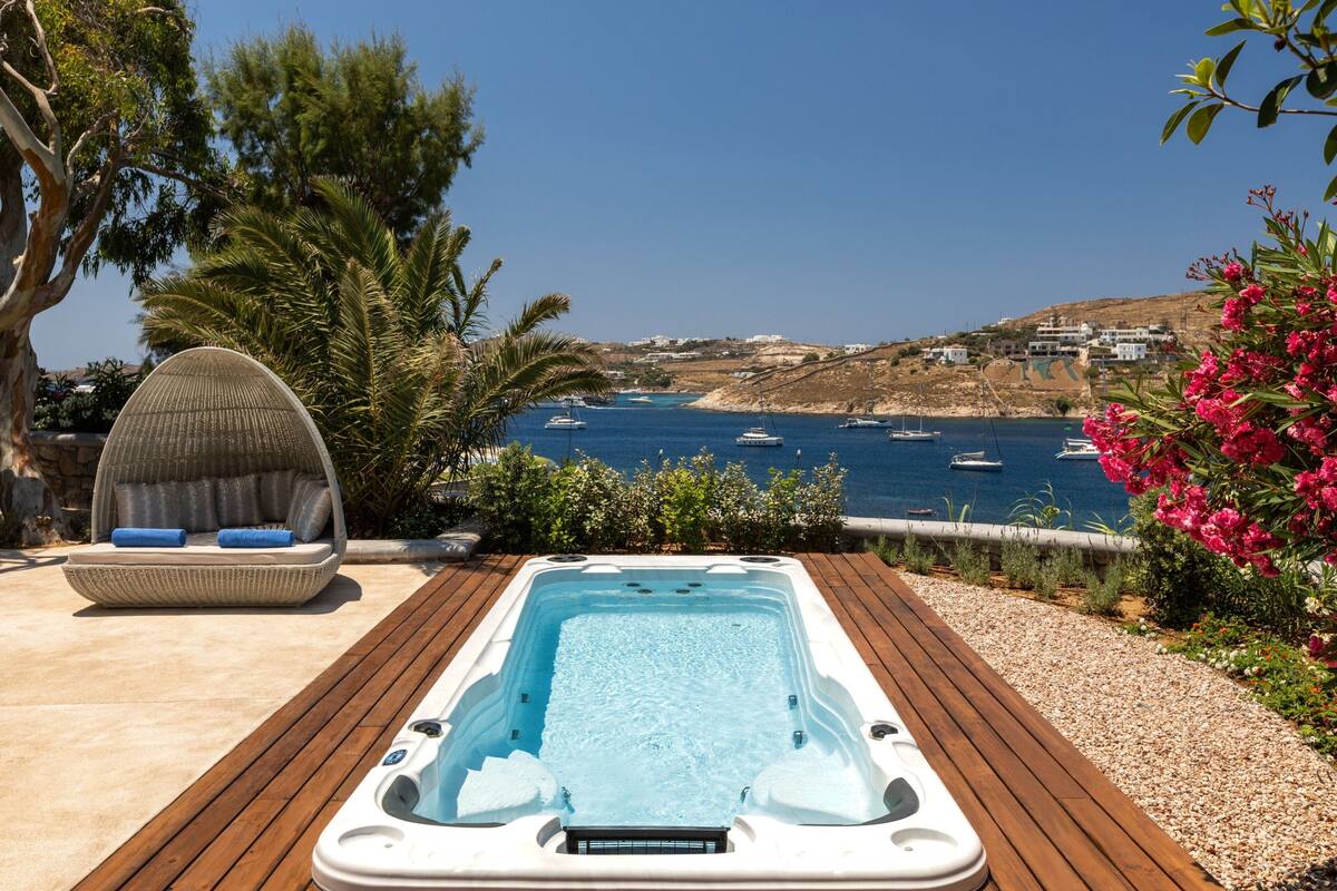 A hot tub on a wooden deck with a view of the sea and boats.
