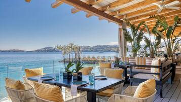 Un restaurante frente al mar con mobiliario de mimbre, techo de madera y vistas al océano.