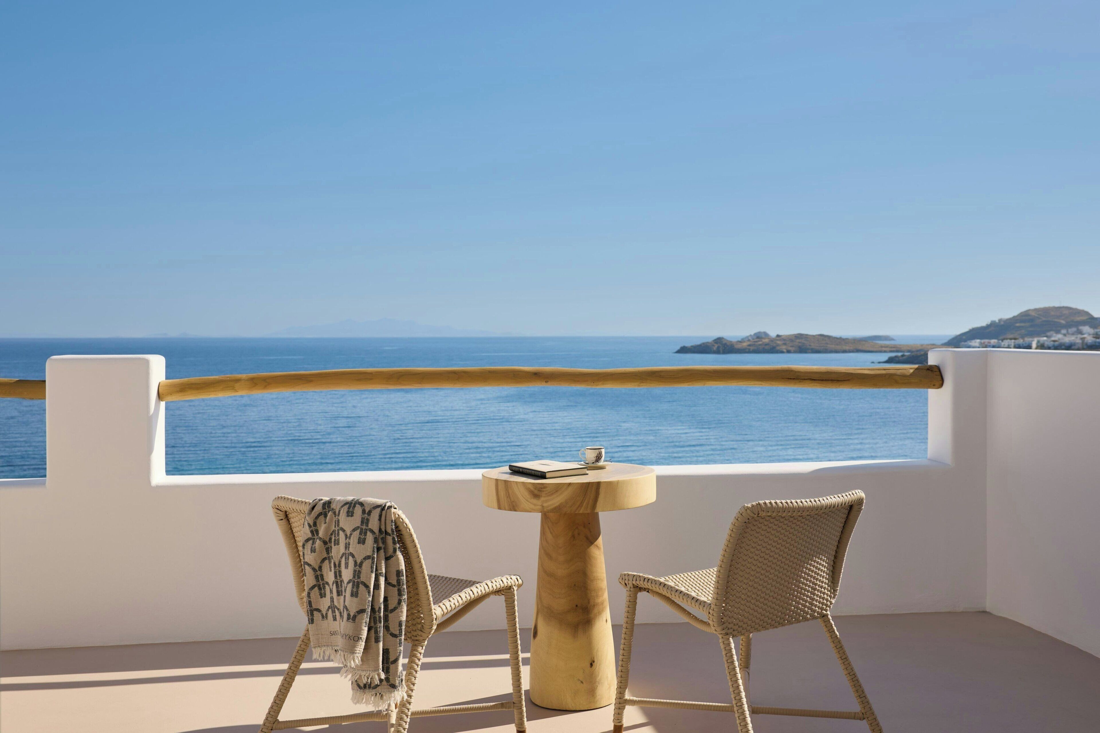 A balcony with two wicker chairs, a round wooden table, and a view of the sea.