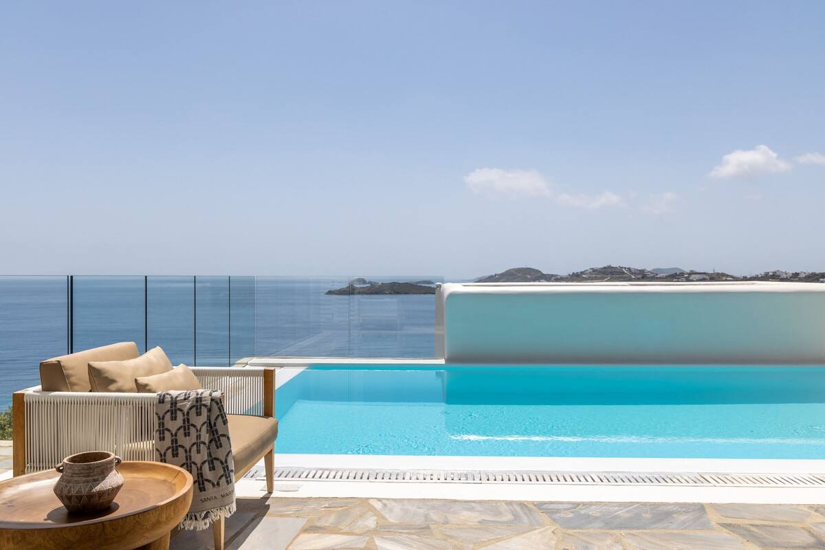 A pool with a clear view of the ocean and a lounge area with a sofa and a table.
