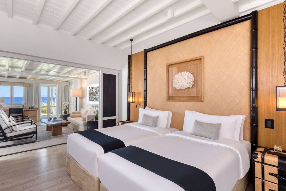 A hotel room with two beds, a large window with a view, a wooden accent wall, and a ceiling with exposed beams.